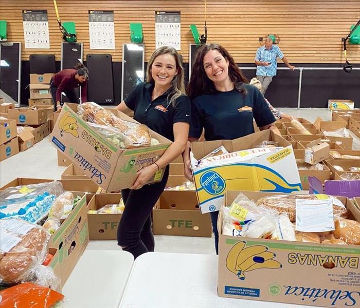Two women holding cardboard boxes containing food. 