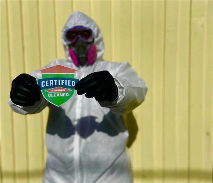 Man in PPE holding up a Certified: Servpro Cleaned sticker