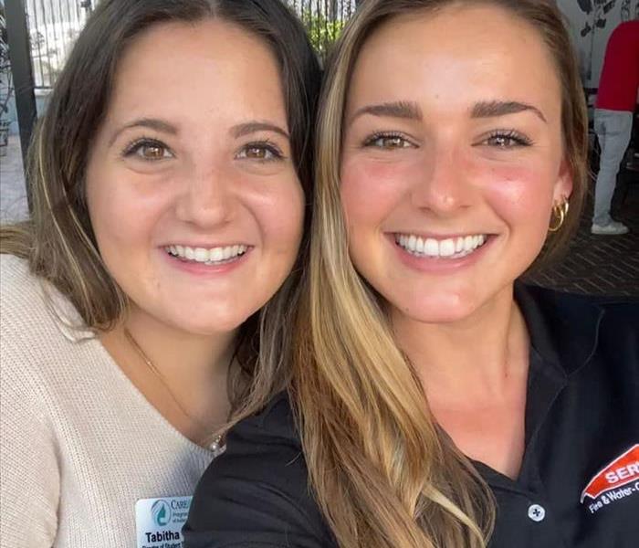 Two women smiling. One is wearing a tan sweater and the other is in a black polo. 