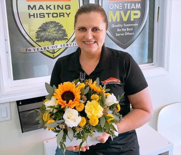Woman with brown hair and black shirt holding a bouquet of sunflowers and other greenery 