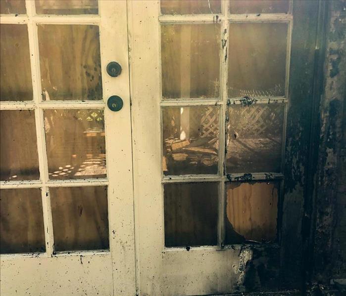 Front of a door burned by fire, and a window pane broken through 