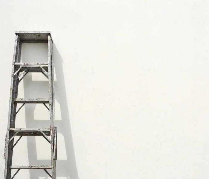 Silver metal ladder propped against a white wall
