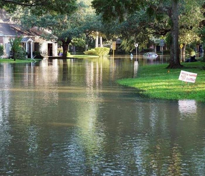 Flooded street with a white home in the background and small patch of green grass on the right hand side