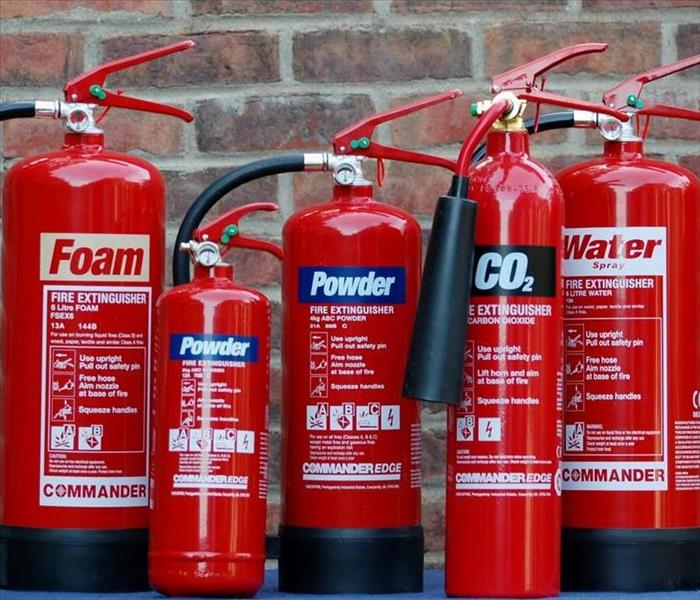 Five fire extinguishers of various sizes lined up in front of a brick wall   