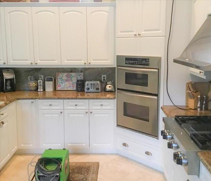 Clean kitchen in home with white cabinets. SERVPRO equipment dehumidifier and air mover are finishing up the work