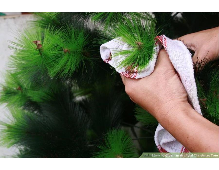 Hands holding a wash cloth while wiping a Christmas tree branch down. 