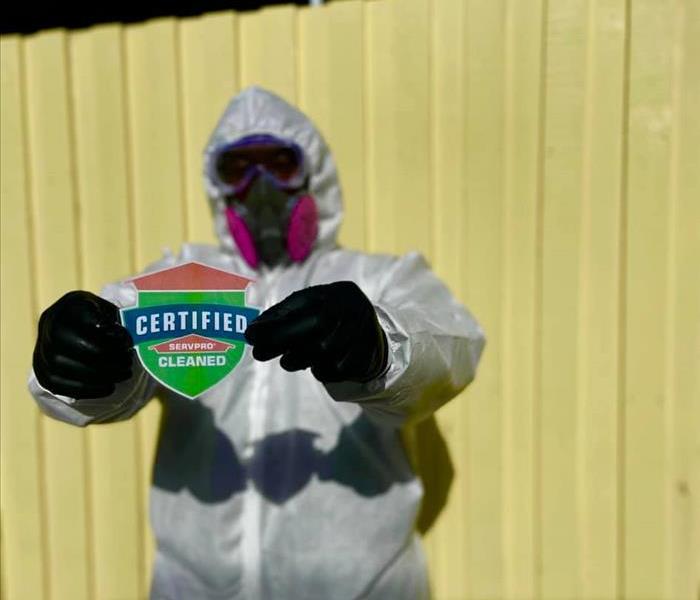 Man in full PPE holding up the Certified: SERVPRO Cleaned shield. 