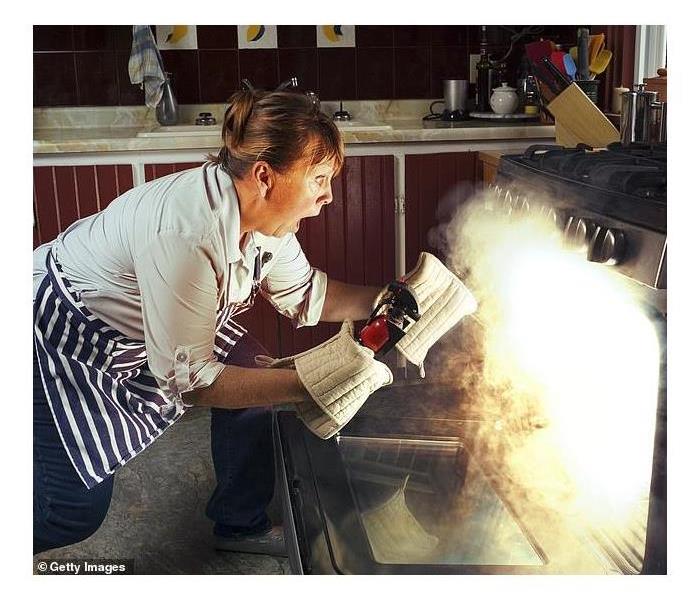 Woman using fire extinguisher to put out an oven fire.