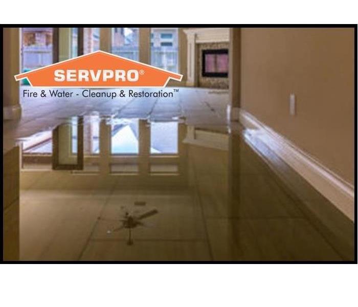 Tile floor leading in to living room with the first half covered in water. SERVPRO logo in top left corner. 