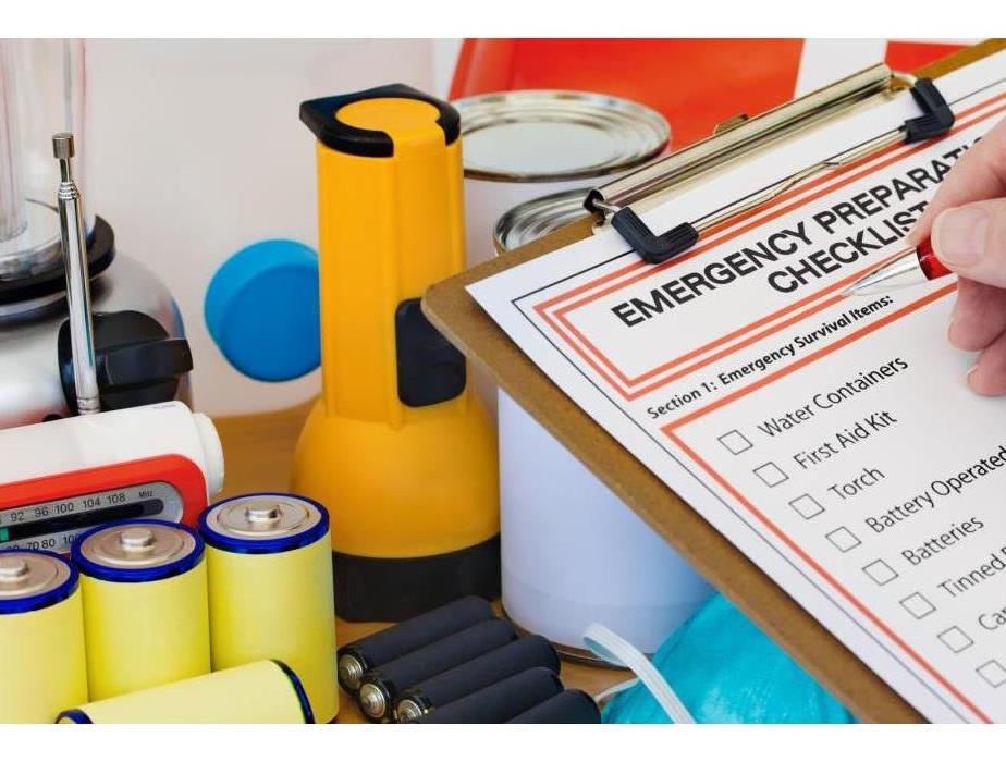 Clip board with disaster supply checklist and flashlights, batteries, and canned foods in the background 
