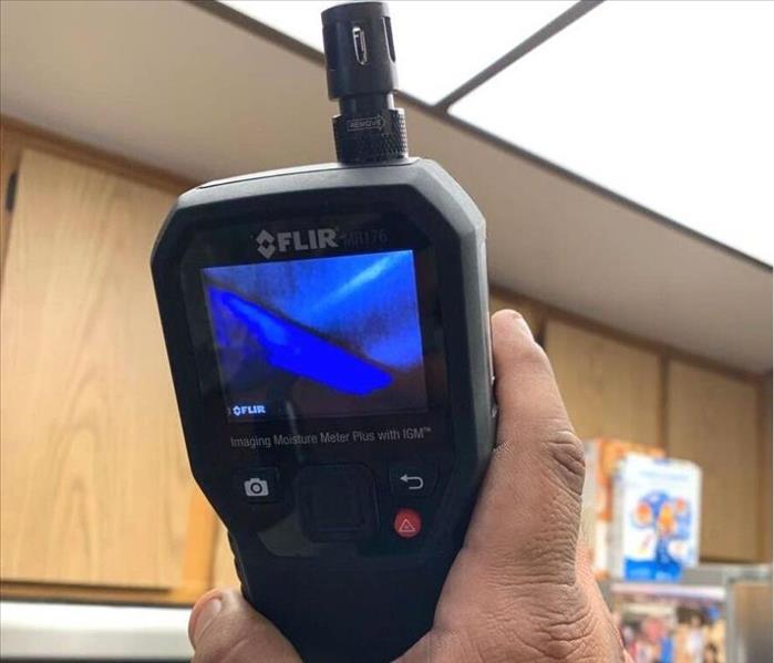 Hand holding up thermal imaging camera to detect a leak in the kitchen ceiling 