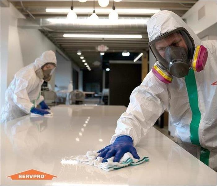 Two workers dressed in PPE wearing respirators while cleaning a table surface. 