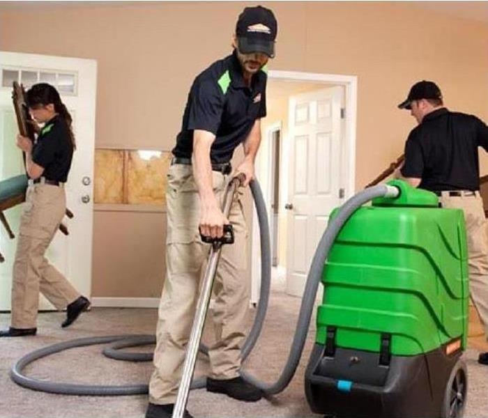 Three SERVPRO employees cleaning a room in a home. Two are moving furniture, the third is cleaning the carpet.